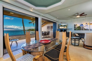 A modern dining area with a glass table, wooden chairs, and a view of the ocean.