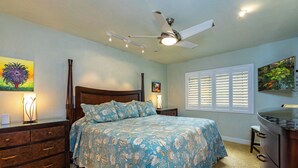 A bedroom with a bed, dresser, nightstand, ceiling fan, and artwork on the walls. - Beachfront Living - Makena Surf E-202 - Mesmerizing Views & Tropical Landscapes (Makena, Maui)