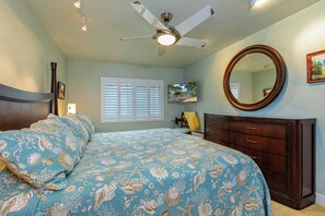 A bedroom with a bed, a ceiling fan, a dresser, a mirror, and a window with blinds. - Beachfront Living - Makena Surf E-202 - Mesmerizing Views & Tropical Landscapes (Makena, Maui)