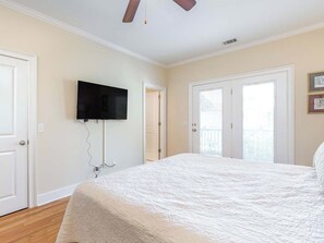 A bedroom with a large bed, a ceiling fan, a mounted TV, and a door leading to a balcony. - Lazy Dayz | Pet Friendly, Great for Large Groups! (Tybee Island)