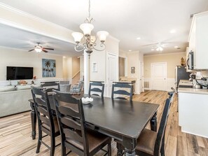 A dining area with a dark wooden table and chairs, a chandelier, and a ceiling fan.