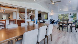 A spacious dining area with a long wooden table and multiple chairs, a kitchen area with wooden cabinets and a stone backsplash, and a cozy living room with a fireplace and comfortable seating.