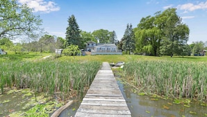A wooden pier leading to a house surrounded by lush greenery and a pond.