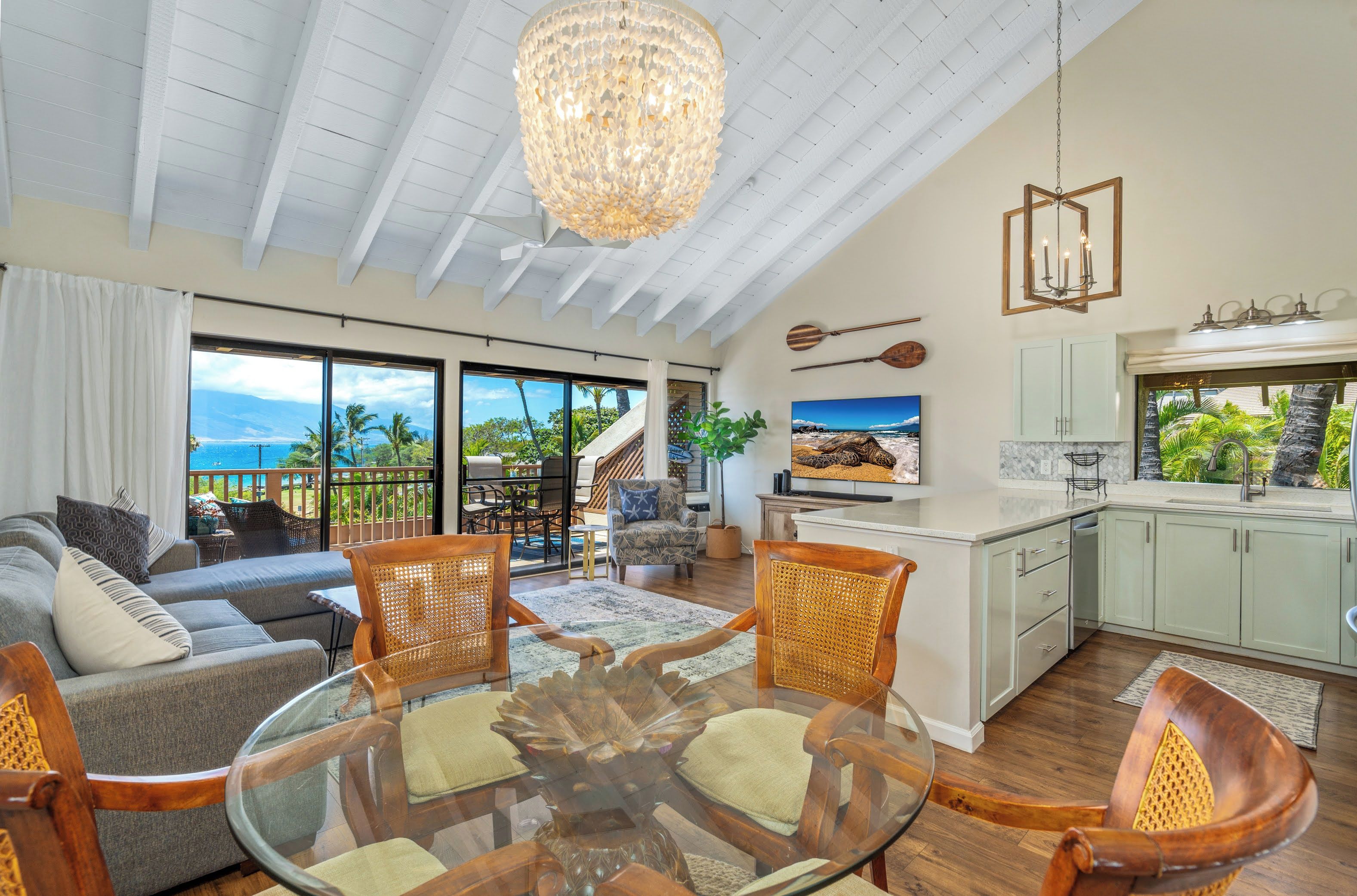 A spacious living area with a glass dining table, comfortable seating, a kitchen with a view, and a balcony overlooking the ocean.