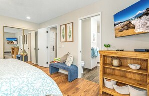 A bedroom with a large bed, a wooden bench, a TV, and a shelf with bowls.