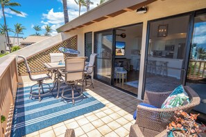 A sunlit patio with a dining area, wicker furniture, and a view of the beach.