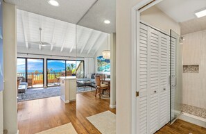 Een ruime woonkamer met een grote schuifpui naar een balkon, een gezellige zithoek met een bank en fauteuils, en een douchecabine met glazen wanden.