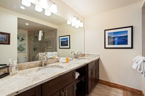 Une salle de bain avec un double lavabo, un grand miroir et des tableaux encadrés accrochés au mur.