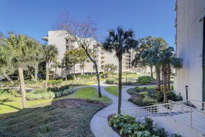 A landscaped courtyard with palm trees, a winding pathway, and a multi-story building with balconies.