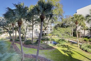 Escape to a serene courtyard surrounded by lush greenery and palm trees, featuring a tranquil pond and modern architecture.