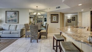 A spacious living room with a sofa, patterned chairs, a dining table, and a kitchen area with a marble countertop and sink.