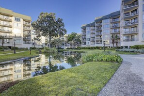 A modern apartment complex with multiple balconies, a central courtyard with a pond, and well-maintained landscaping.