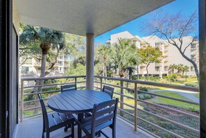 A balcony with a table and chairs, overlooking a landscaped area with palm trees and a building in the background.