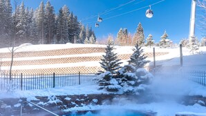 A hot spring surrounded by snow-covered trees and a ski lift in the background.