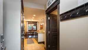 A hallway leading to a kitchen area with a dining table and chairs, a wooden door, and a coat rack with hooks.