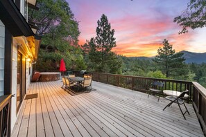 A wooden deck with outdoor furniture, a red umbrella, and a scenic view of trees and mountains during sunset. - Knotting Hill | Mountain Views, Spa & Fenced Deck (Idyllwild)