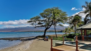 A beach with a wooden deck, a pool, and a chair.