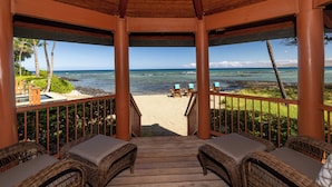 A wooden deck with wicker furniture overlooking a beach.