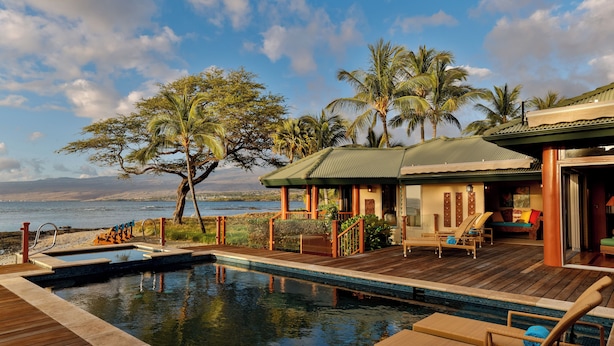 A poolside area with lounge chairs, a wooden deck, and a view of the ocean.