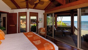 A bedroom with a large bed, a ceiling fan, and a view of the ocean through a sliding glass door.