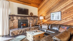 A cozy living room with a stone fireplace, leather sofa, and a television mounted on the wall. - Beautiful Spacious Pet-Friendly Townhome 264 (Mammoth Lakes)