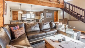 A spacious living room with a leather sectional sofa, a wooden coffee table, and a staircase leading to an upper level. - Beautiful Spacious Pet-Friendly Townhome 264 (Mammoth Lakes)