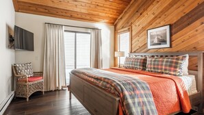 A wooden-paneled bedroom with a bed, curtains, a chair, and a mounted TV. - Beautiful Spacious Pet-Friendly Townhome 264 (Mammoth Lakes)