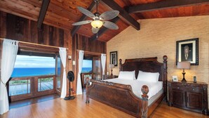A wooden-framed bedroom with a large bed, a ceiling fan, and a view of the ocean. - 🏖️Amazing Ocean Views | Infinity Pool | Great Location (Kailua Kona)