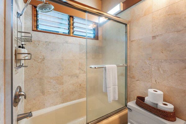 A modern bathroom with a glass shower enclosure, a toilet with a basket of toiletries, and a towel rack.