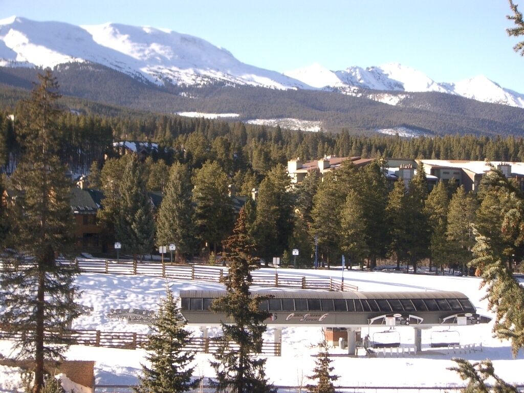 A ski resort with a covered area, snow-covered ground, and a mountainous backdrop.