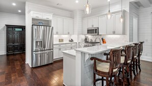 Cozinha moderna com armários brancos, eletrodomésticos de aço inoxidável e uma ilha central com banquetas.