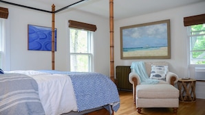 A bedroom with a bed, a chair, a painting of a beach, and a window with a view of trees. - Aurora Escape: "Spectacular Design Awaits You!" (Aurora)