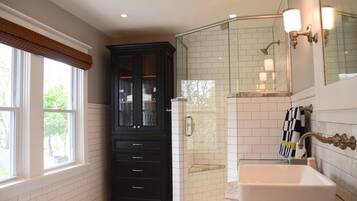 Une salle de bain avec un meuble en bois foncé, une cabine de douche en verre et un lavabo blanc.