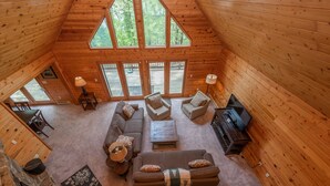 A cozy cabin interior with a large wooden ceiling, a sectional sofa, two armchairs, a coffee table, and a fireplace. - Deep Creek Dog Friendly Cabin w/ Dock & Fireplace (Swanton)