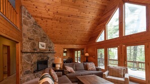 A log cabin interior with a stone fireplace, wooden ceiling, and large windows. - Deep Creek Dog Friendly Cabin w/ Dock & Fireplace (Swanton)