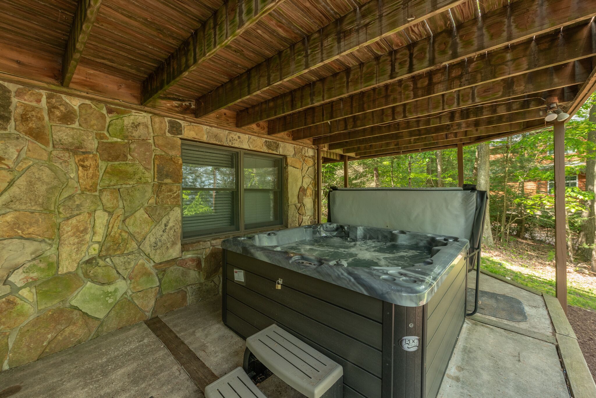 Un bain à remous sous un toit en bois, entouré de murs en pierre et doté d’une fenêtre.