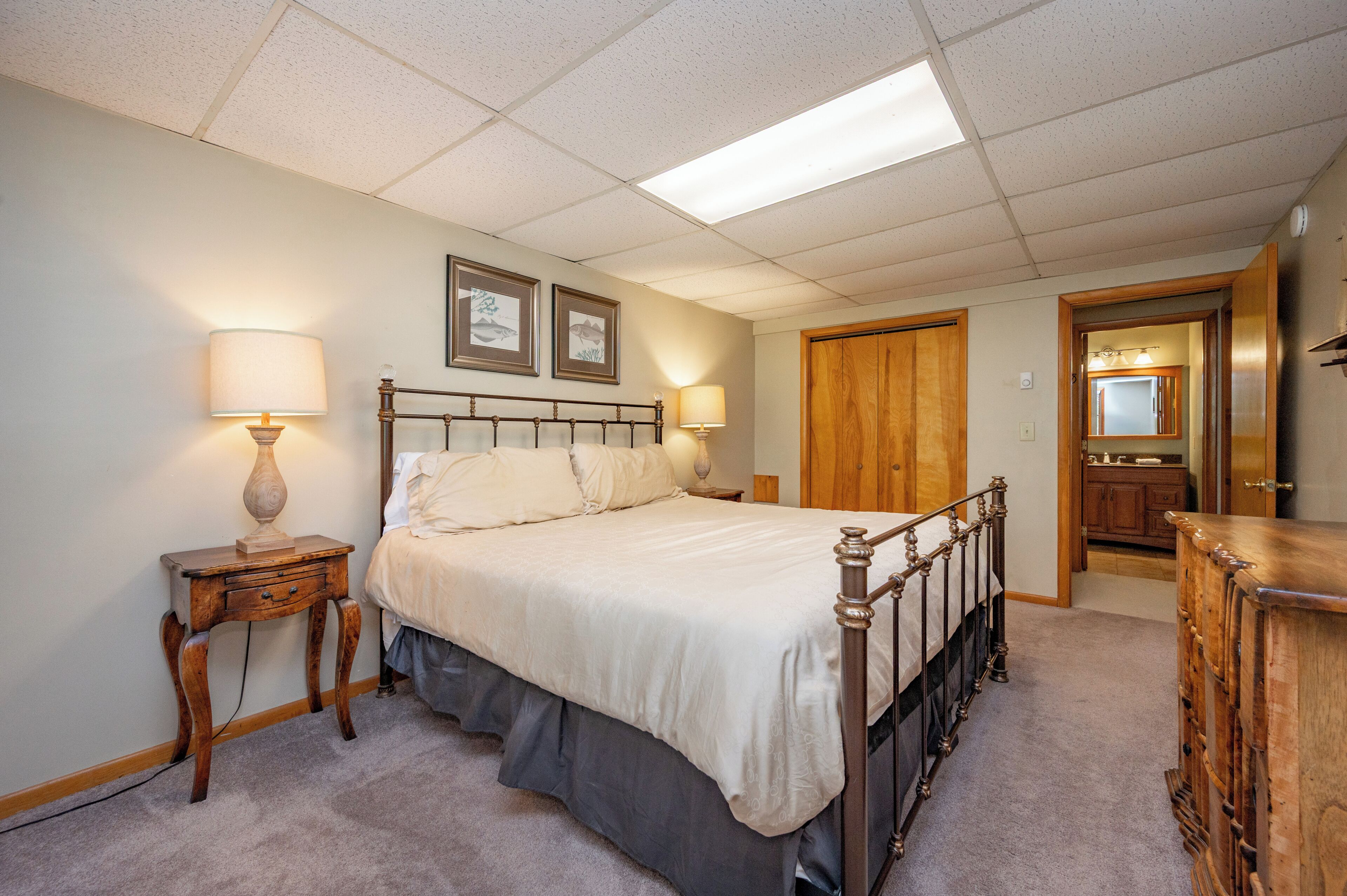 A bedroom with a bed, bedside lamps, a wooden dresser, and a door leading to another room.