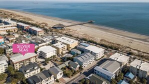 Eine Küstenlandschaft mit einer Mole, die ins Meer ragt, umgeben von Gebäuden und einem Strand.