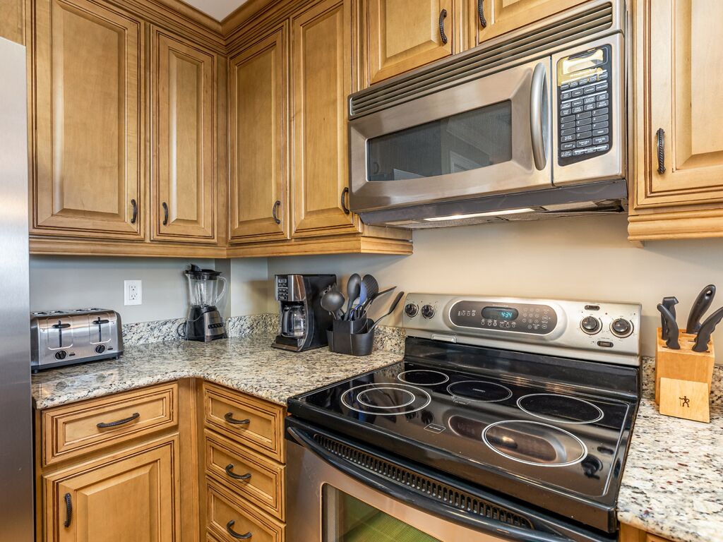A kitchen with wooden cabinets, a stainless steel microwave, a stove, and a toaster.