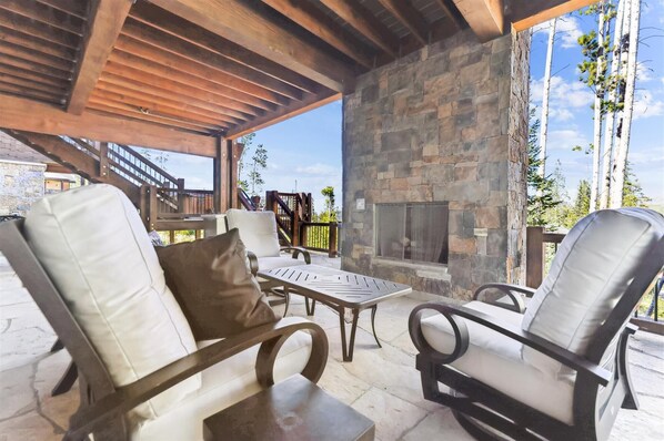Un patio exterior con suelo de piedra, chimenea de piedra y mobiliario de madera.