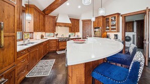 Een keuken met houten kasten, een wit eiland en blauwe bekleden barkrukken.