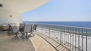 Een balkon met een tafel en stoelen, met uitzicht op een strand met geparkeerde auto's en parasols.