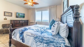 Un dormitorio con una cama grande, un ventilador de techo, un aparador y vista al océano.