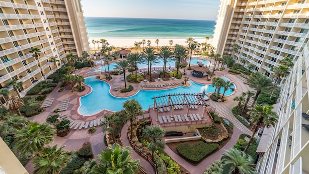Un resort con varias piscinas, palmeras y vista a la playa.