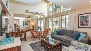 Ein geräumiges Wohnzimmer mit großem Fenster zum Strandblick, ein Essbereich mit Korbstühlen und einem Deckenventilator.