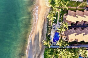 An aerial view of a resort with a beach, a swimming pool, and palm trees.