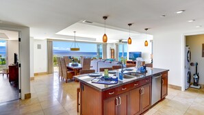 Uma cozinha espaçosa com uma ilha grande, luminárias pendentes modernas e vista para o oceano.