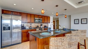 Uma cozinha moderna com armários de madeira, eletrodomésticos de aço inoxidável, uma ilha grande com banquetas e iluminação pendente.