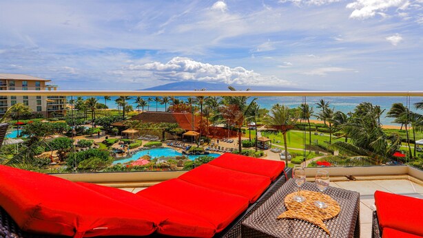 Uma varanda com almofadas vermelhas, piscina e vista para a praia e o oceano.