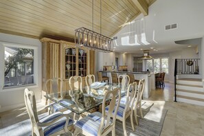 A spacious dining area with a glass table and striped chairs, a kitchen with modern appliances, and a staircase with a black railing.